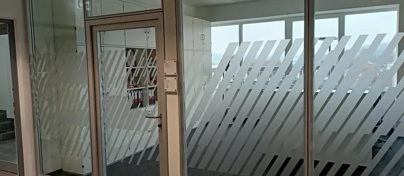Bürotrakt mit Glastrennwänden und diagonalem Streifendesign aus Milchglasfolie, Blick über den Flur
