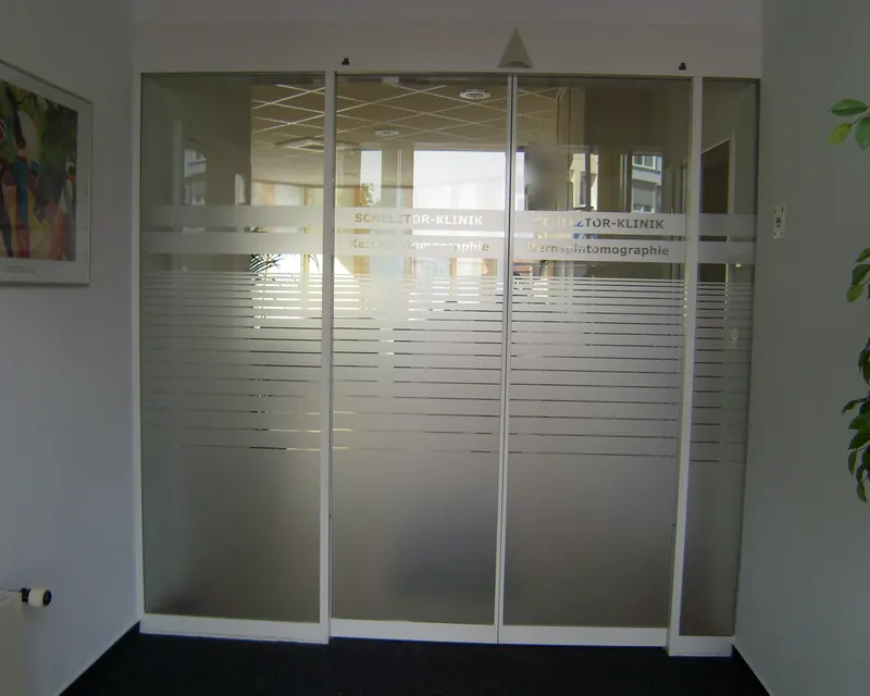 Automatische Glasschiebetür in einer Klinik mit Markierungsband, Beschriftung und Streifenverlauf