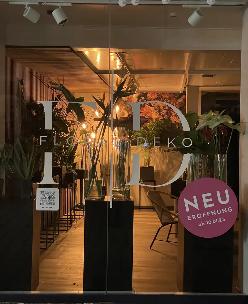 Schaufenster eines Blumengeschäfts mit großem weißem Logo-Monogramm und rundem Eröffnungs-Aufkleber