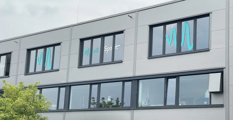 Obergeschoss-Fenster eines Firmengebäudes mit großem Logo-Schriftzug über mehrere Fenster