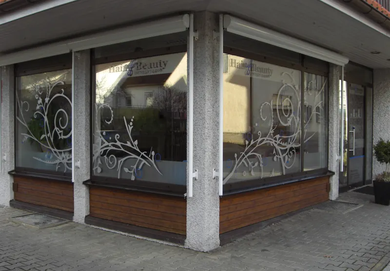 Eckschaufenster eines Friseursalons mit weißem Ornament-Dekor und Milchglasband auf dem Glas