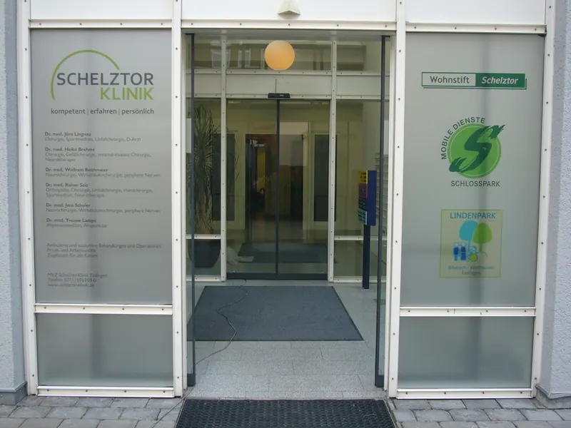 Eingang einer Klinik mit mattierten Glasfeldern, Logos und Ärzteliste als Folienbeschriftung