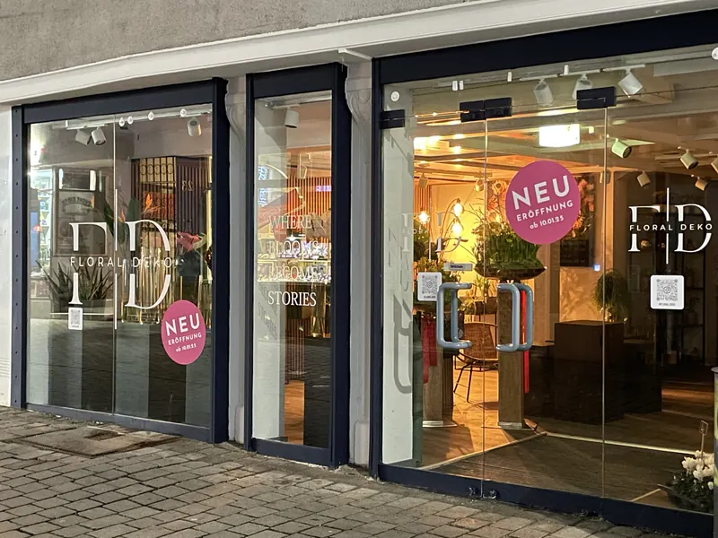 Ladenfront mit weißer Logo-Beschriftung, Schriftzug und Aktionsaufklebern auf allen Glasflächen