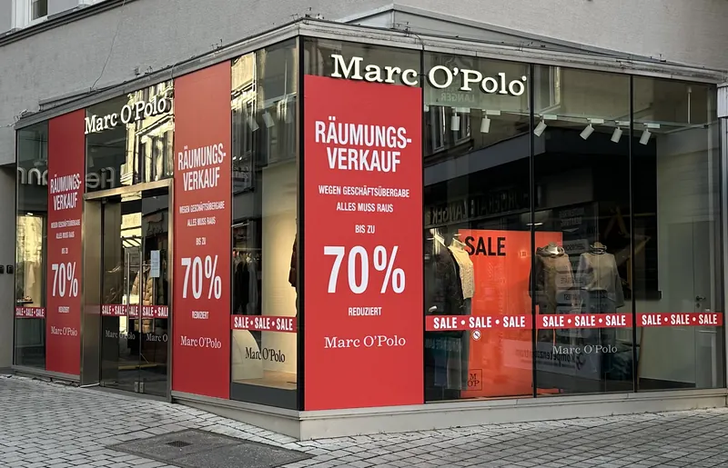 Eckschaufenster eines Modegeschäfts, beide Fensterseiten mit großflächiger Aktionsbeschriftung