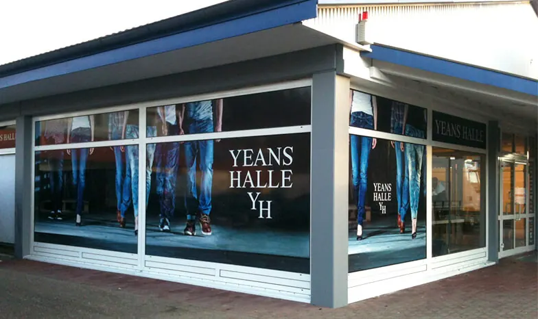 Eckladen eines Modegeschäfts, Schaufenster rundum mit großformatigem Fotodruck und Logo beklebt