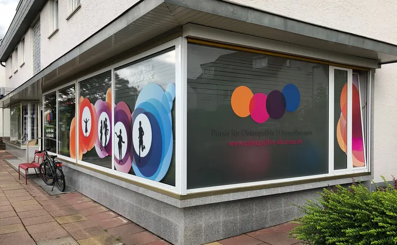 Eckschaufenster einer Praxis mit farbigem Kreis-Design im Digitaldruck und Schriftzug