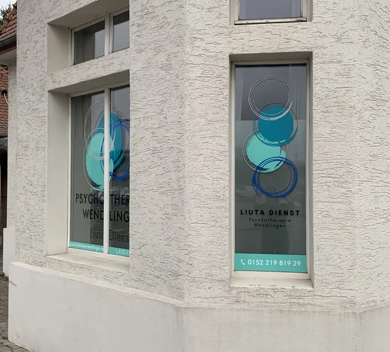 Eckfenster einer Psychotherapie-Praxis mit Milchglasfolie, farbigem Kreis-Motiv und Kontaktdaten