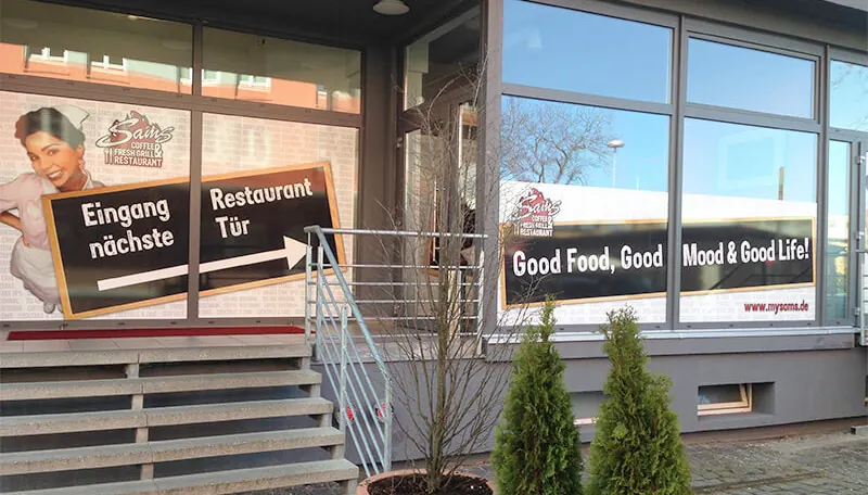Restaurant mit Fensterbeschriftung, Wegweiser zum Eingang und Slogan auf den Scheiben