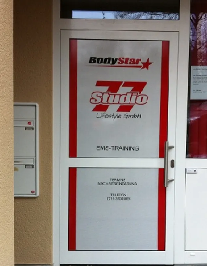 Eingangstür eines Fitnessstudios mit bedruckter Lochfolie: von außen Logo und Kontaktdaten