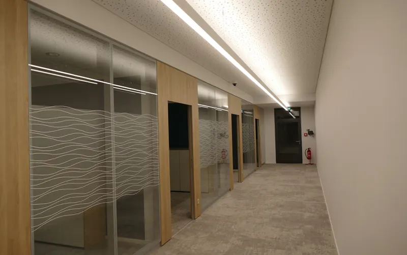 Büroflur mit mehreren Glaswänden, alle mit demselben Wellenmuster beklebt